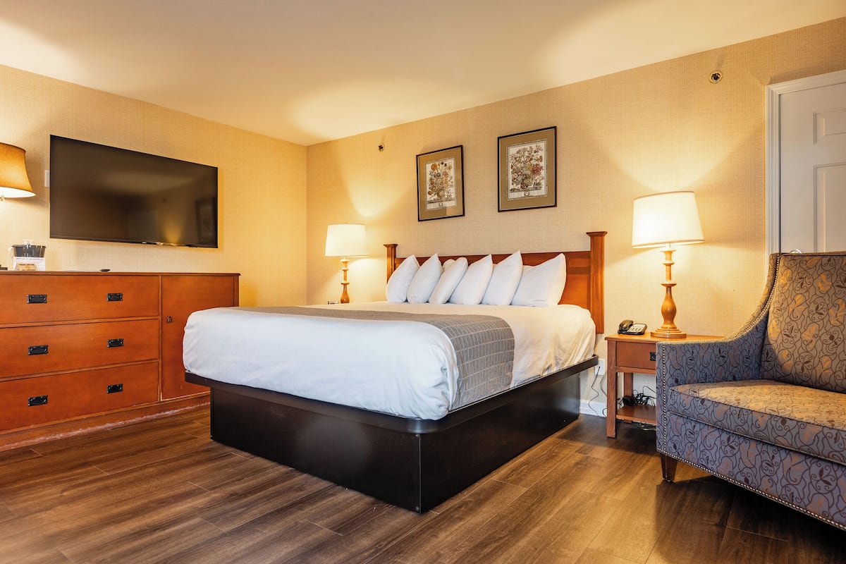 A hotel room with a bed, a chair, a TV, and a dresser.