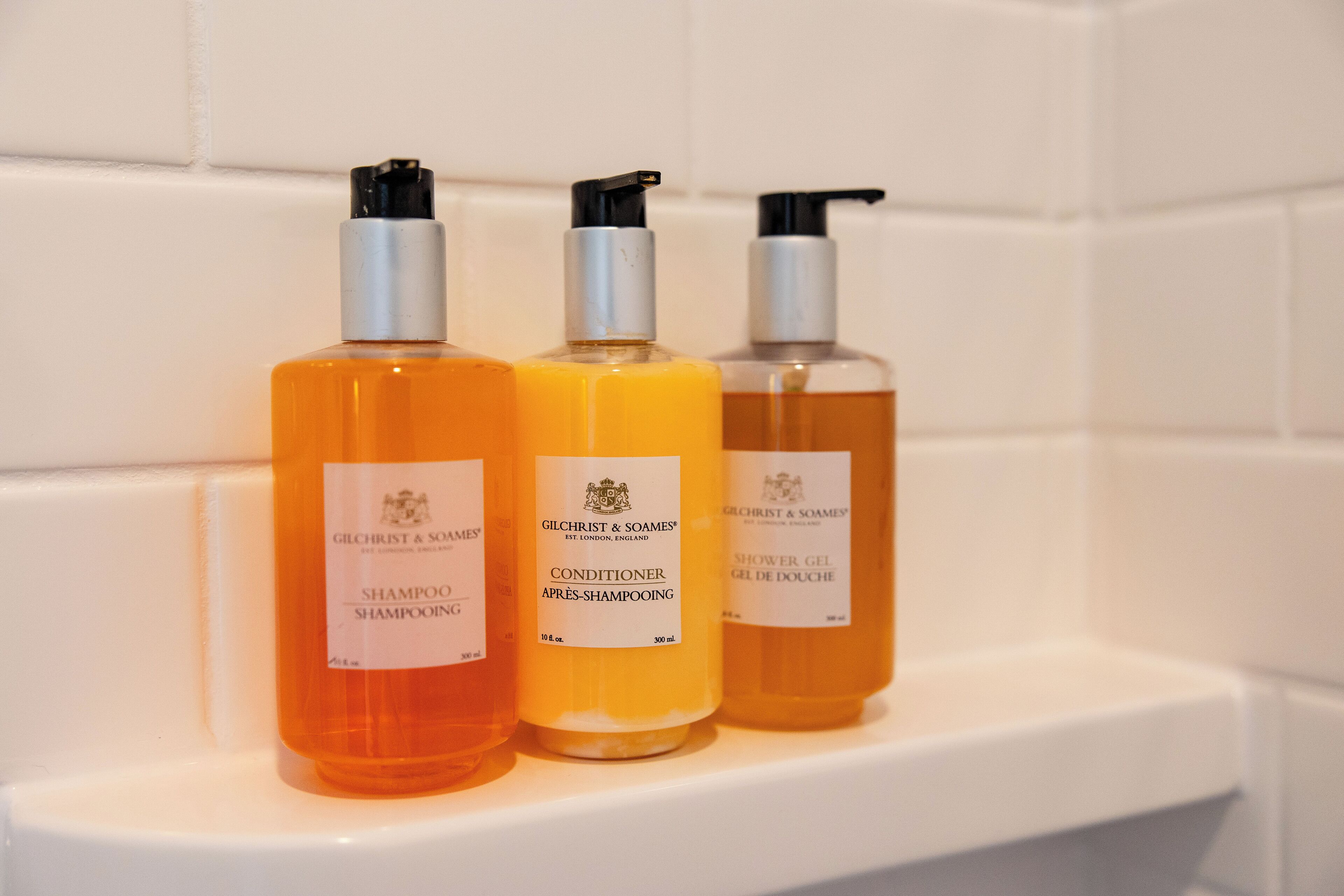 Tres botellas de productos Gilchrist & Soames sobre una estantería blanca.