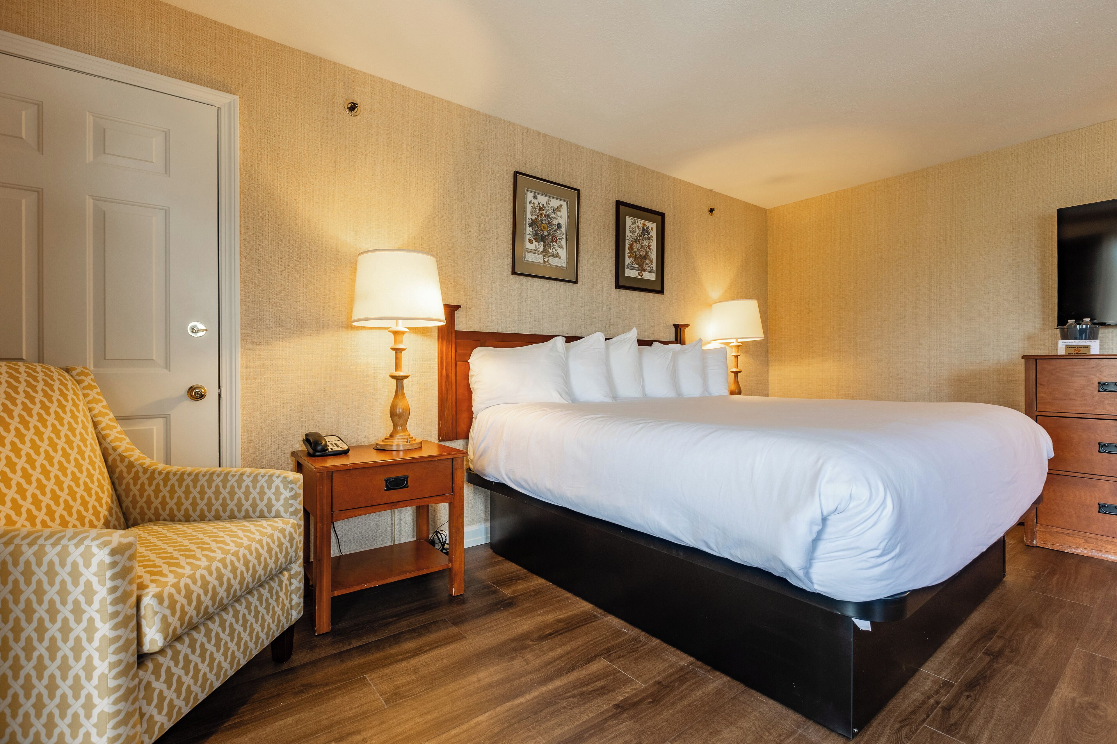 A hotel room with a bed, bedside tables, a chair, a television, and framed pictures on the wall.