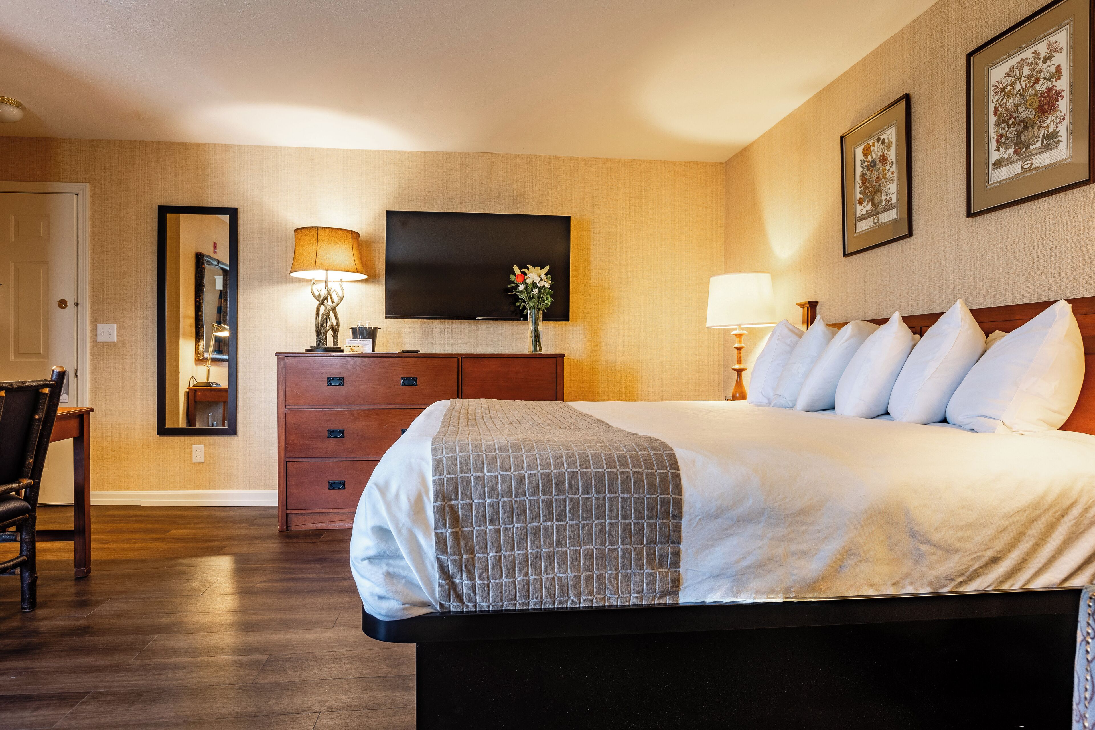 A hotel room with a bed, a television, a dresser, a chair, and framed pictures on the wall.