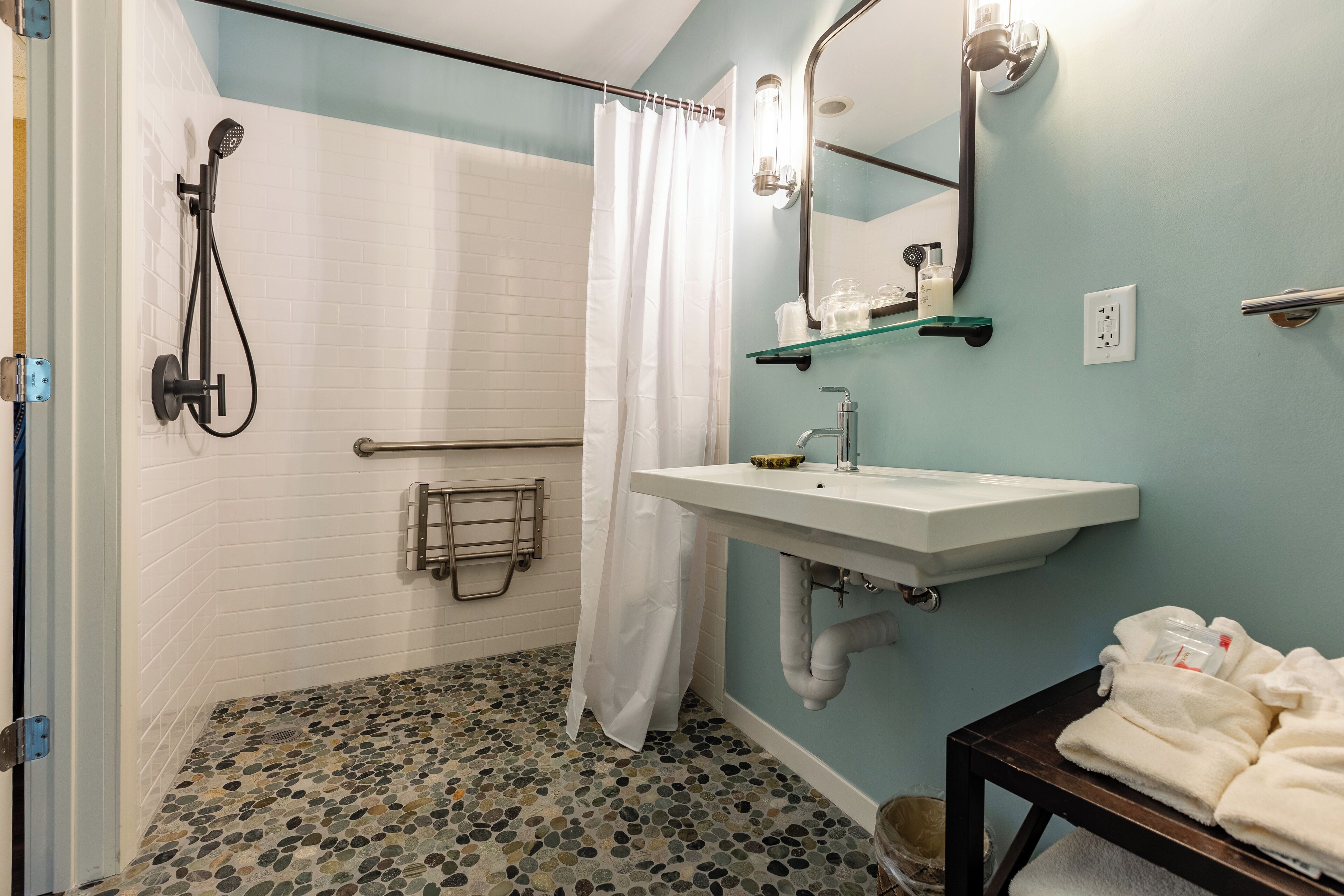 A bathroom with a shower, a sink, a mirror, and a towel rack.