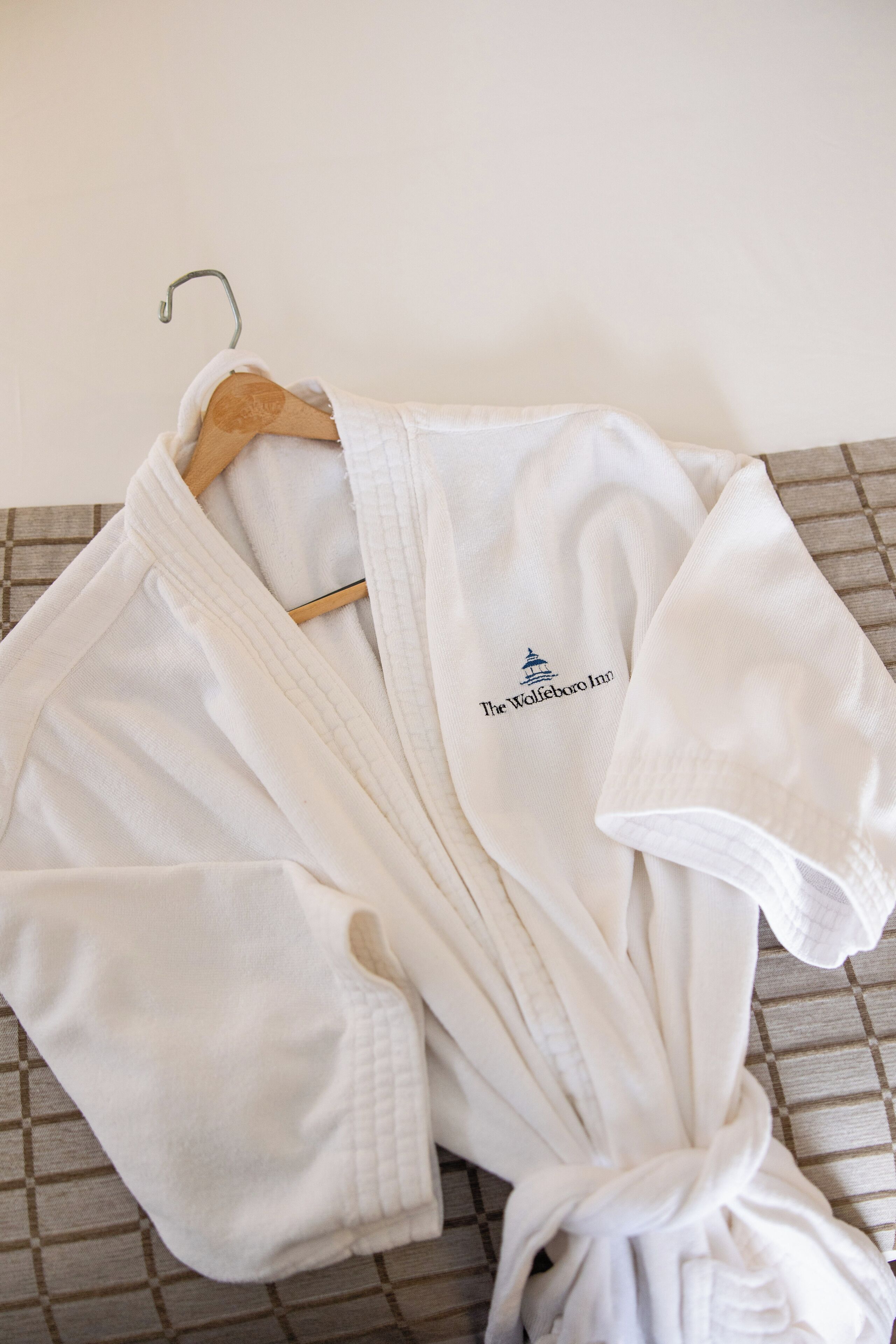 A white robe with a logo on the chest, hanging on a wooden hanger.