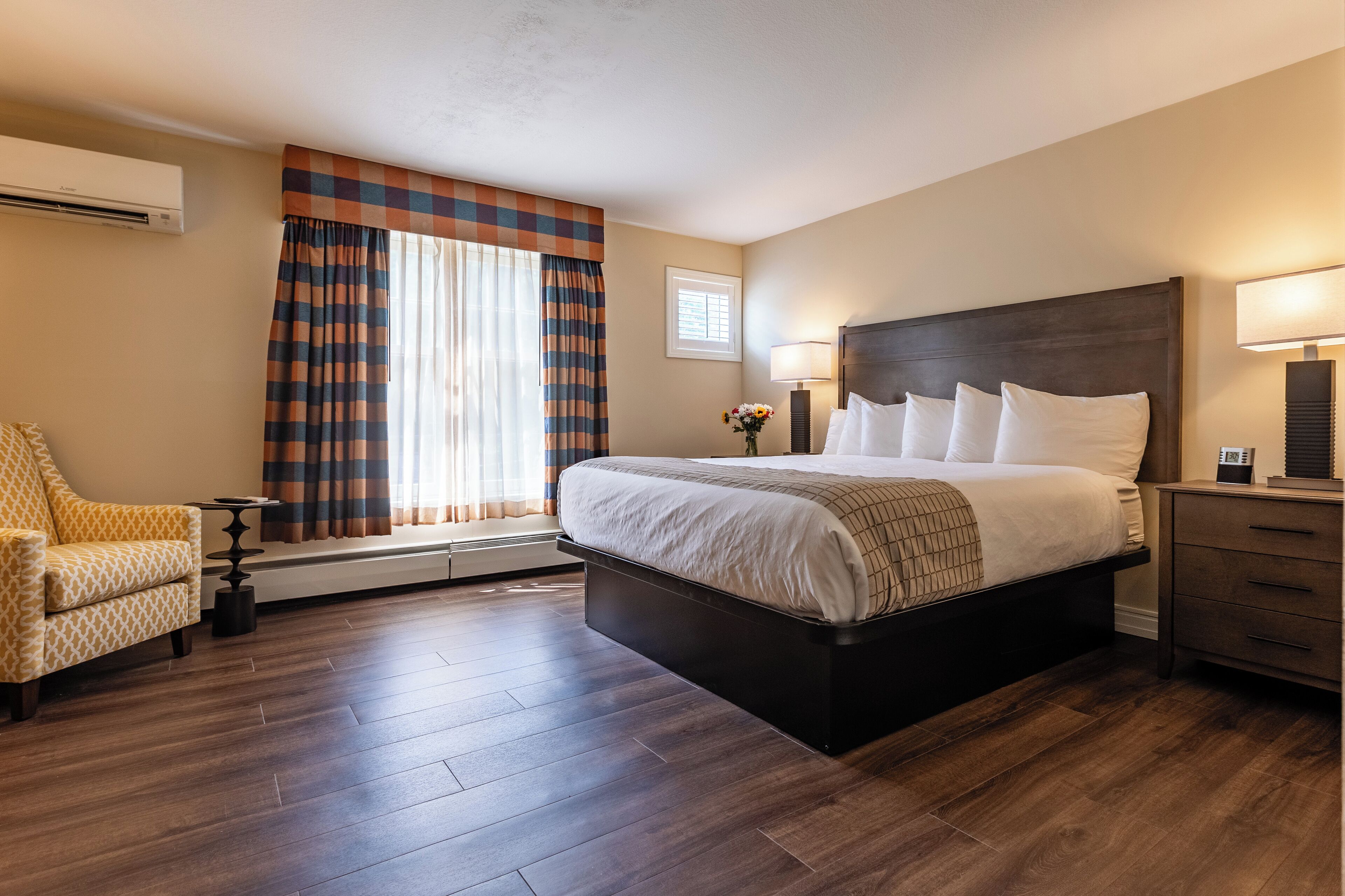 A hotel room with a large bed, a chair, a small table, and a nightstand.