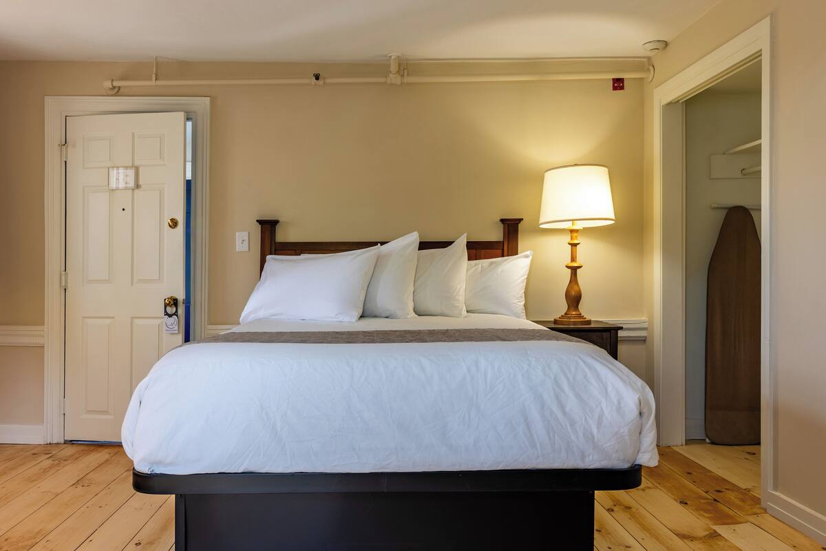 A neatly made bed with white linens, a wooden headboard, and a bedside table with a lamp.