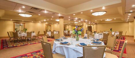 A banquet hall with multiple round tables, each set with white tablecloths, chairs, and centerpieces.