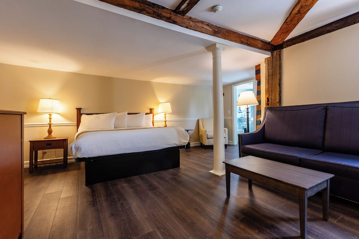 A hotel room with a bed, a sofa, a wooden table, and two bedside lamps.