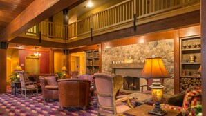 A spacious lobby with a high ceiling, wooden beams, a patterned carpet, leather armchairs, a stone fireplace, and a balcony. - The Wolfeboro Inn (Wolfeboro)