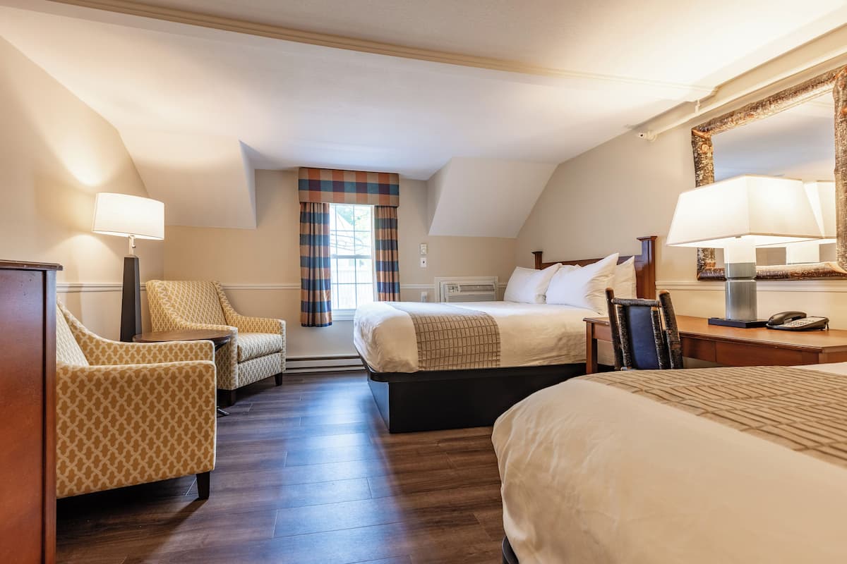 A hotel room with a large bed, two armchairs, a desk with a lamp, a telephone, and a mirror.