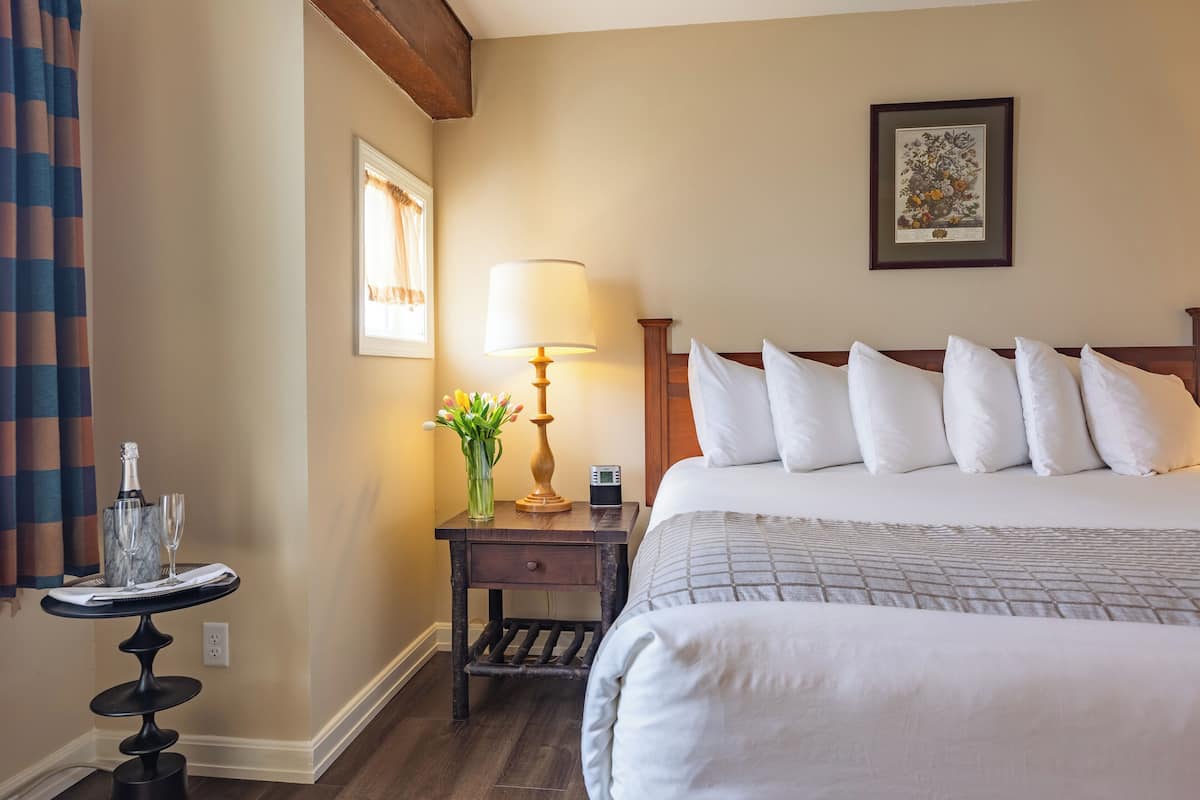 A hotel room with a large bed, a bedside table with a lamp, a framed picture on the wall, and a small table with a vase of flowers.
