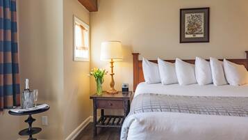 A hotel room with a large bed, a bedside table with a lamp, a framed picture on the wall, and a small table with a vase of flowers.
