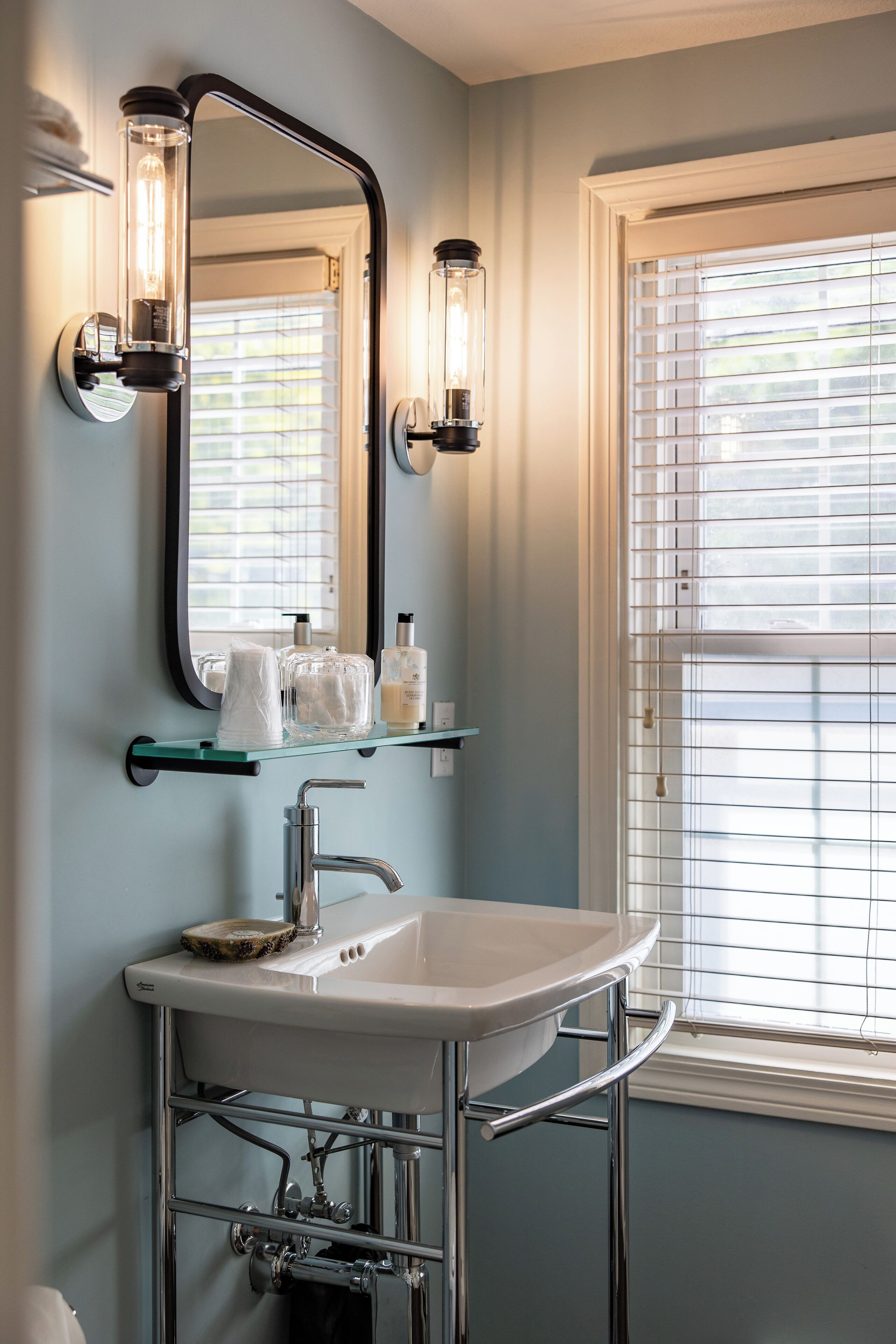 A bathroom with a white sink, chrome fixtures, and a large mirror with wall sconces.