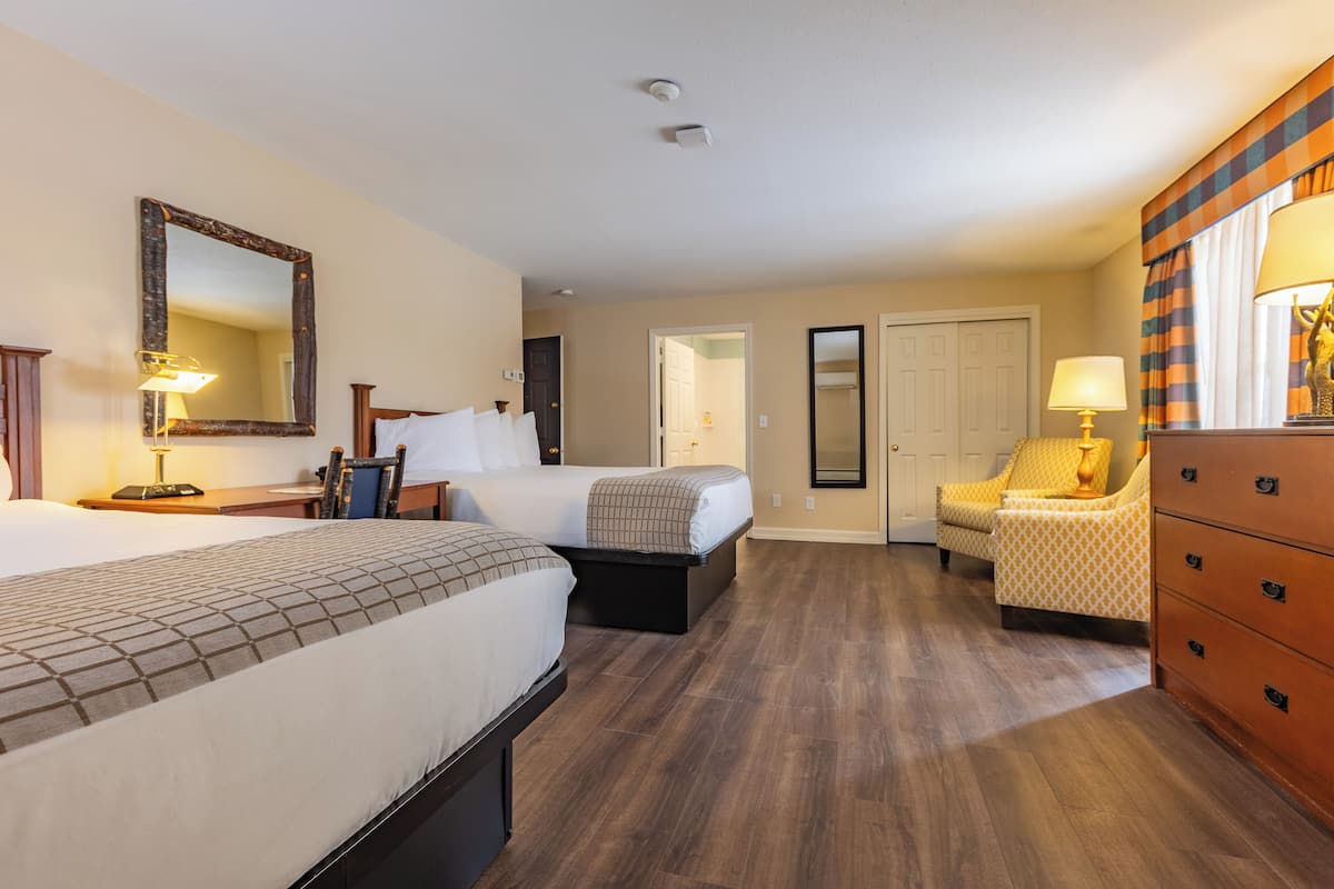 A hotel room with two beds, a chair, a dresser, and a mirror.