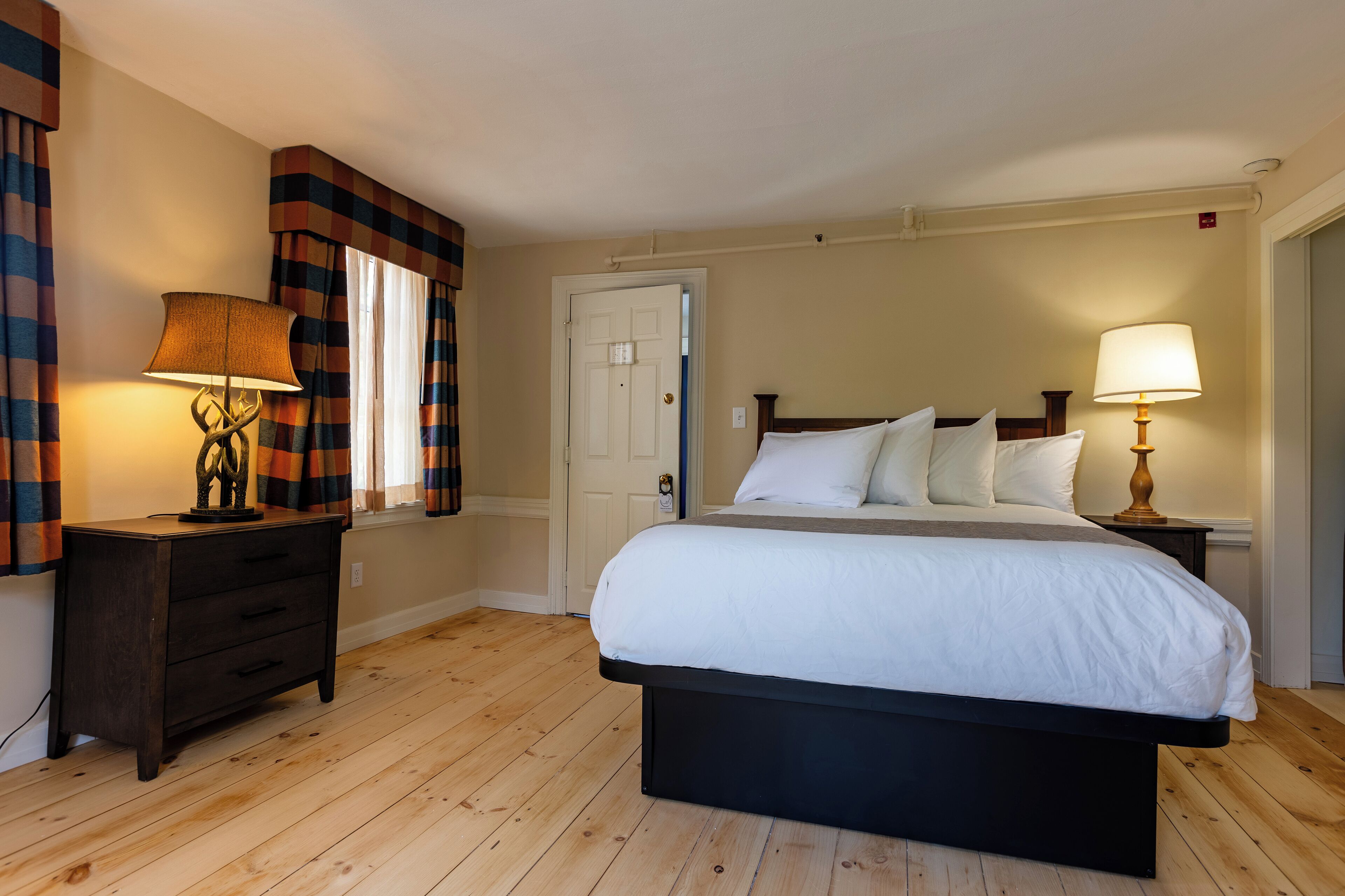 Een slaapkamer met een groot bed, twee nachtkastjes met lampen, een houten vloer en een deur.