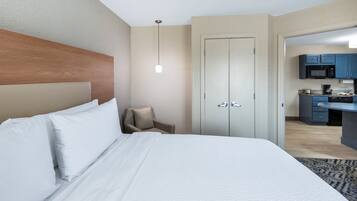 A hotel room with a bed, a chair, a desk, and a kitchenette.