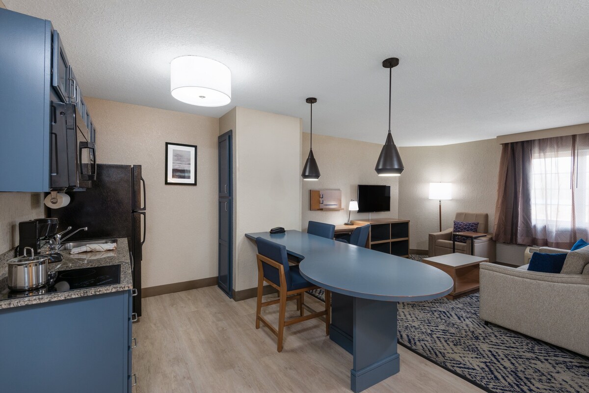 Una cocina compacta con una isla central, una zona de comedor con sillas, un sofá y un televisor.