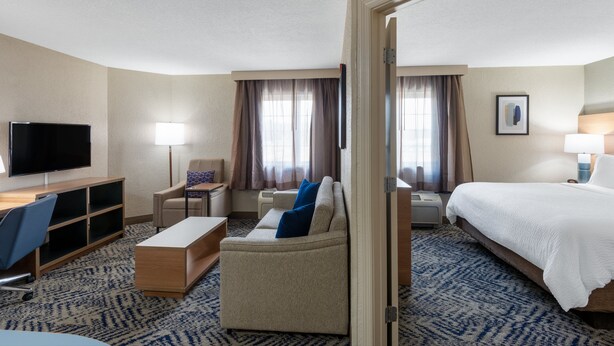 A hotel room with a bed, a sofa, a desk with a chair, a television, and a window with curtains. - Candlewood Suites Chesapeake/Suffolk by IHG (Chesapeake)