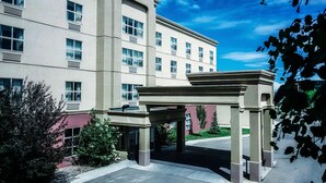 A multi-story hotel with a central entrance pavilion, large windows, and a clear sky. - Hampton Inn & Suites by Hilton Edmonton Intl Airport (Leduc)
