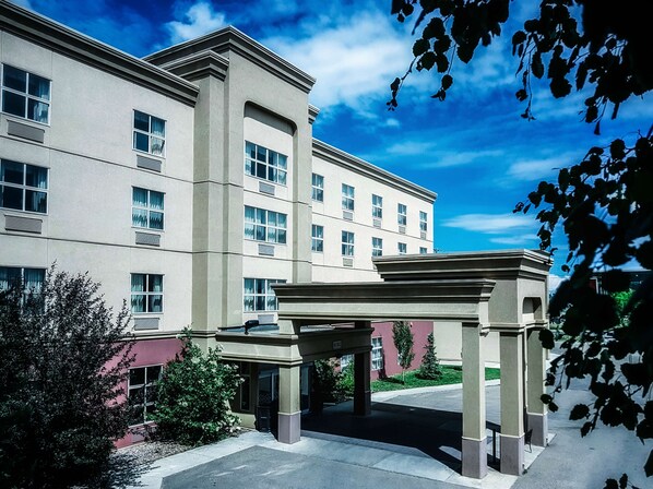 A multi-story hotel with a central entrance pavilion, large windows, and a clear sky. - Hampton Inn & Suites by Hilton Edmonton Intl Airport (Leduc)