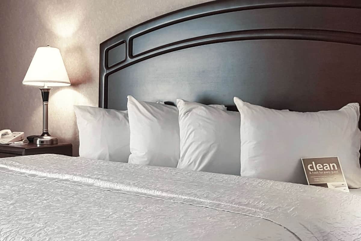 A neatly made bed with white linens and pillows, a bedside lamp, and a sign indicating the room is clean.