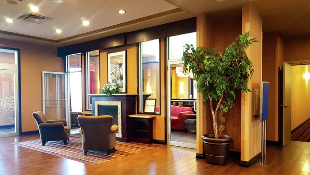 A spacious lobby with a wooden floor, a seating area with chairs, a potted plant, and a fireplace. - Hampton Inn & Suites by Hilton Edmonton Intl Airport (Leduc)