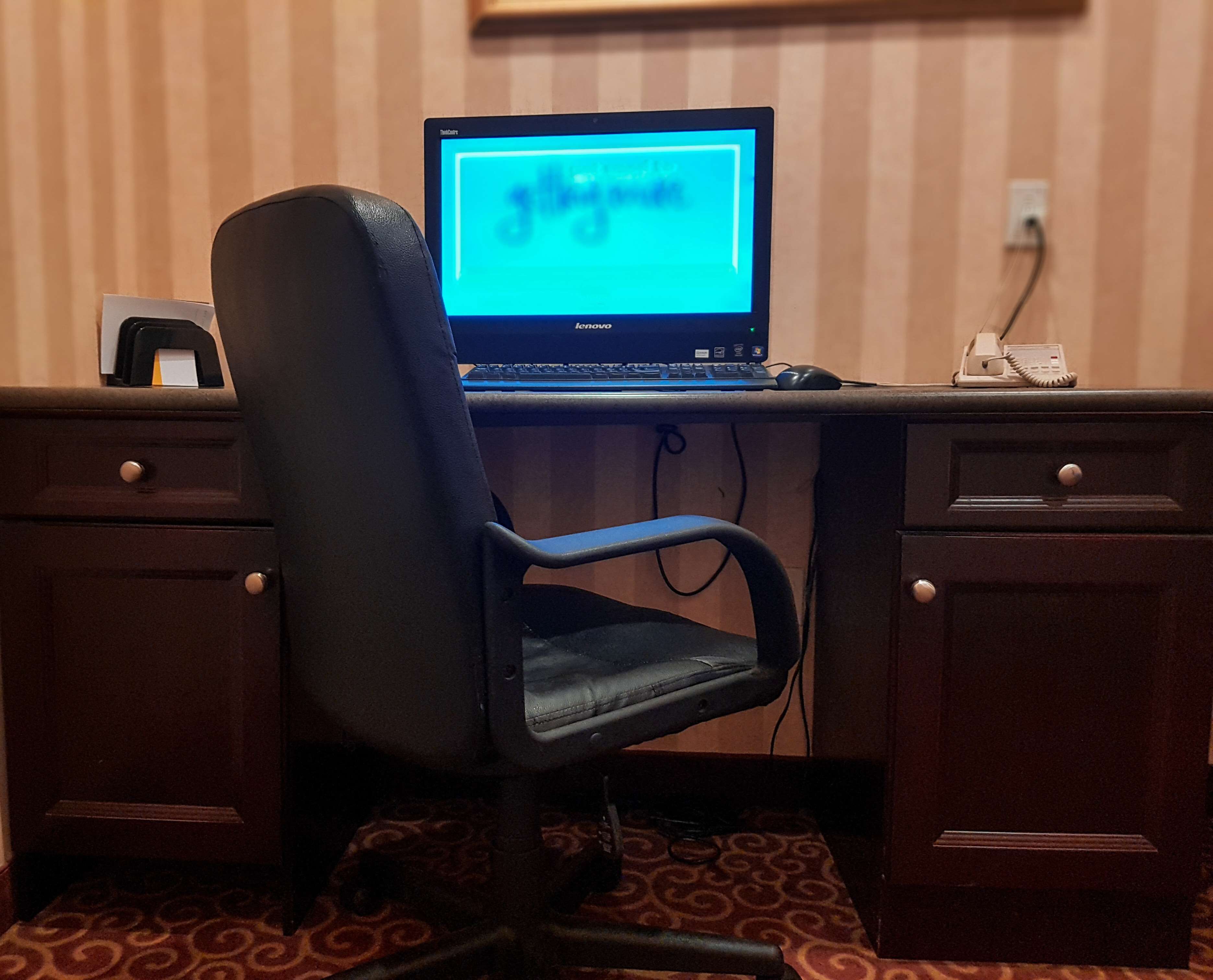 A laptop on a desk with a chair, a telephone, and a wall socket.