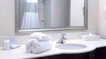 Une salle de bain d’hôtel avec un grand miroir, un lavabo et un porte-serviettes.