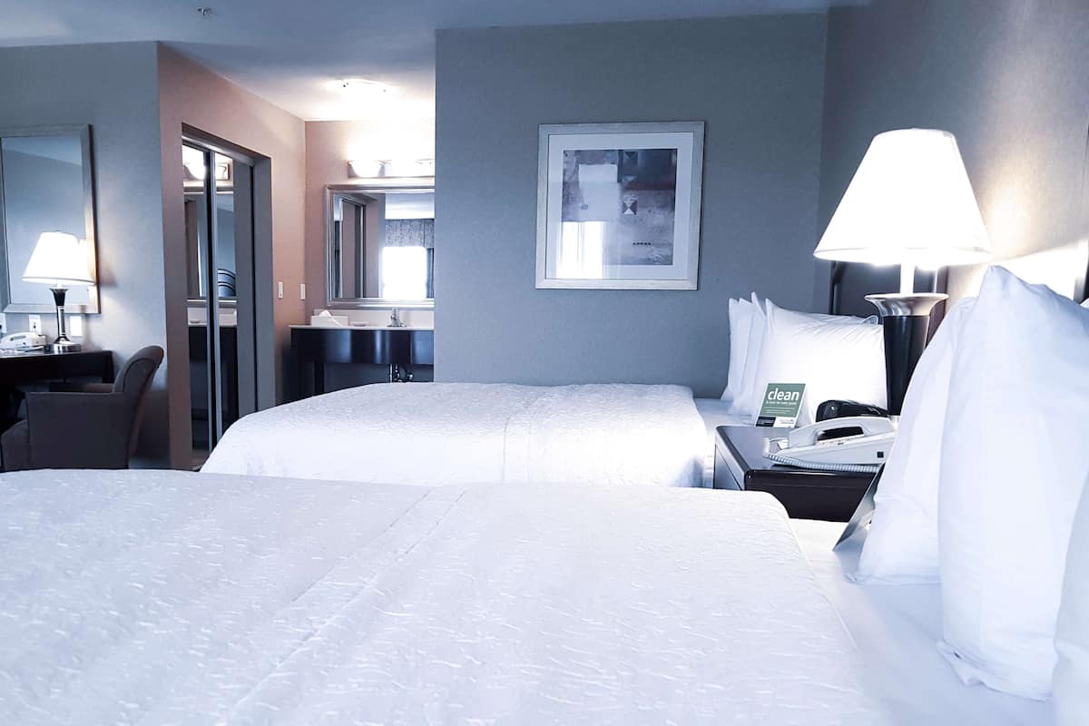 A hotel room with two beds, a desk with a lamp, a mirror, and a framed picture on the wall.
