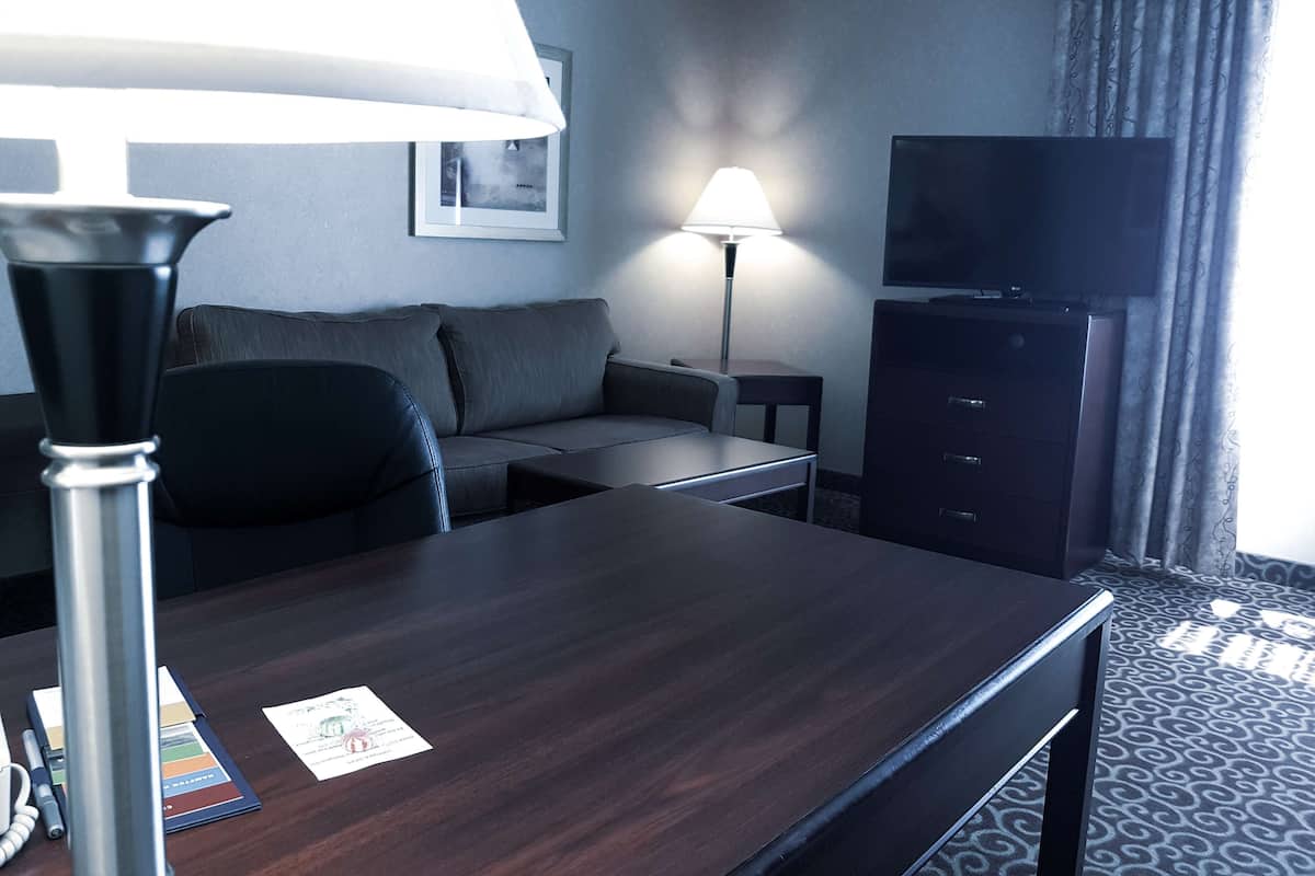A hotel room with a dark wooden desk, a sofa, a lamp, a TV, and a patterned carpet.