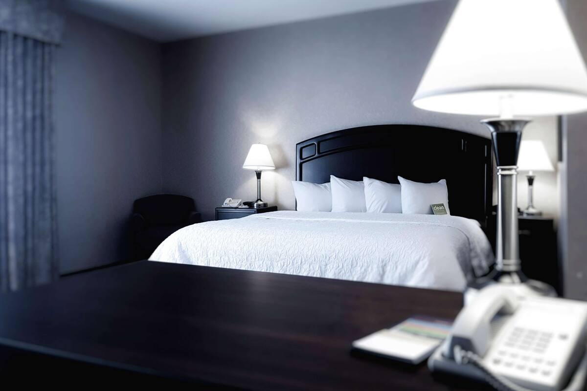 A hotel room with a large bed, two bedside lamps, a bedside phone, and a dark wooden nightstand.