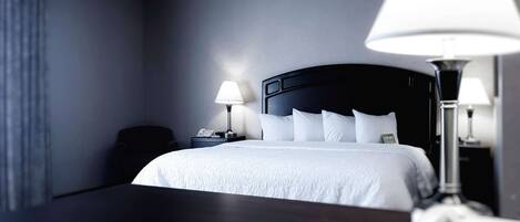 A hotel room with a large bed, two bedside lamps, a bedside phone, and a dark wooden nightstand.