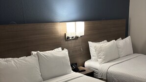 A hotel room with two beds, a nightstand with a phone, and a wall-mounted light fixture.