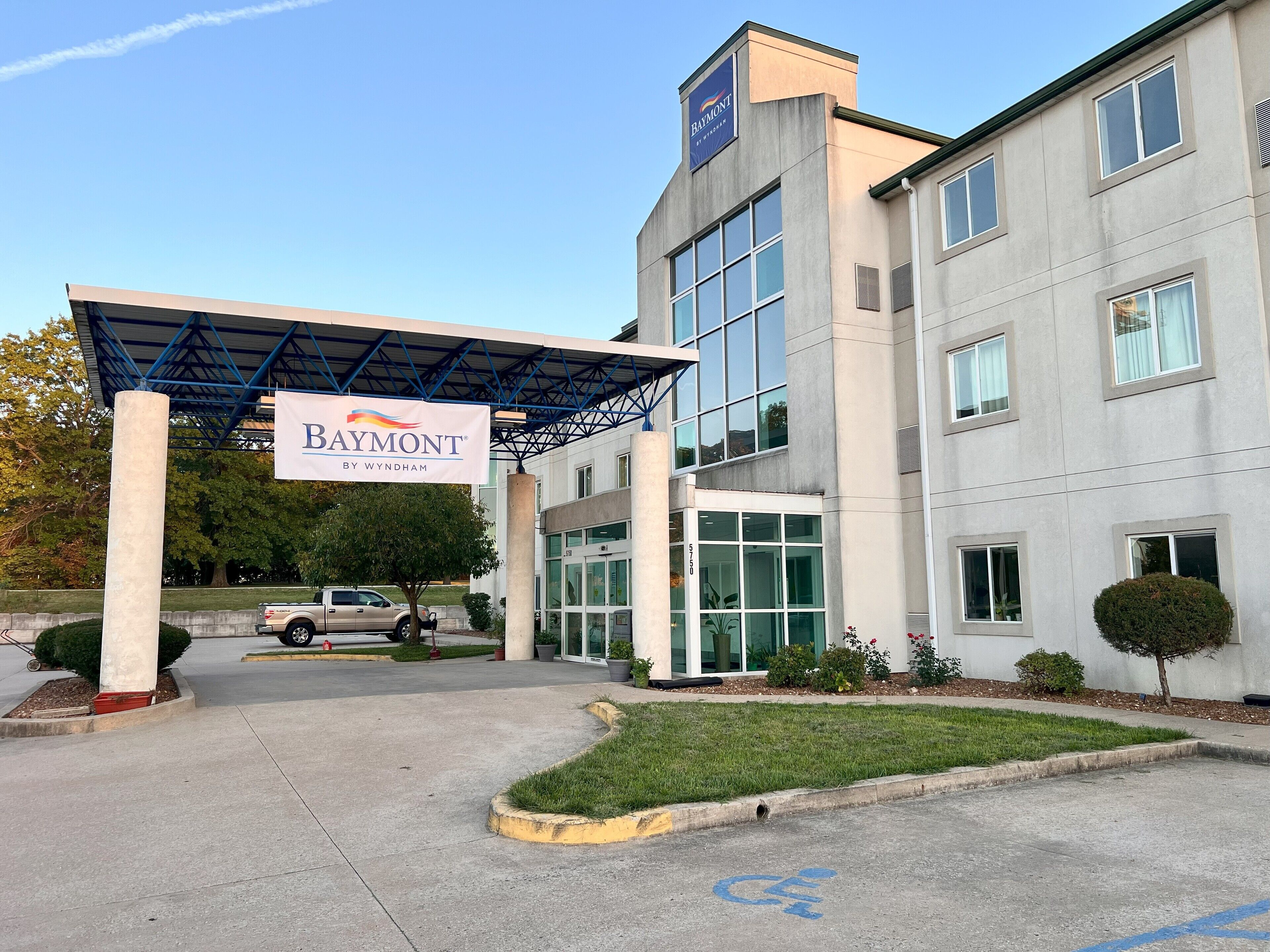 Un edificio moderno con entrada cubierta, un letrero de 'Baymont by Wyndham' y un área de estacionamiento con espacio para sillas de ruedas.