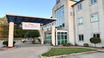 Un edificio moderno con entrada cubierta, un letrero de 'Baymont by Wyndham' y un área de estacionamiento con espacio para sillas de ruedas.