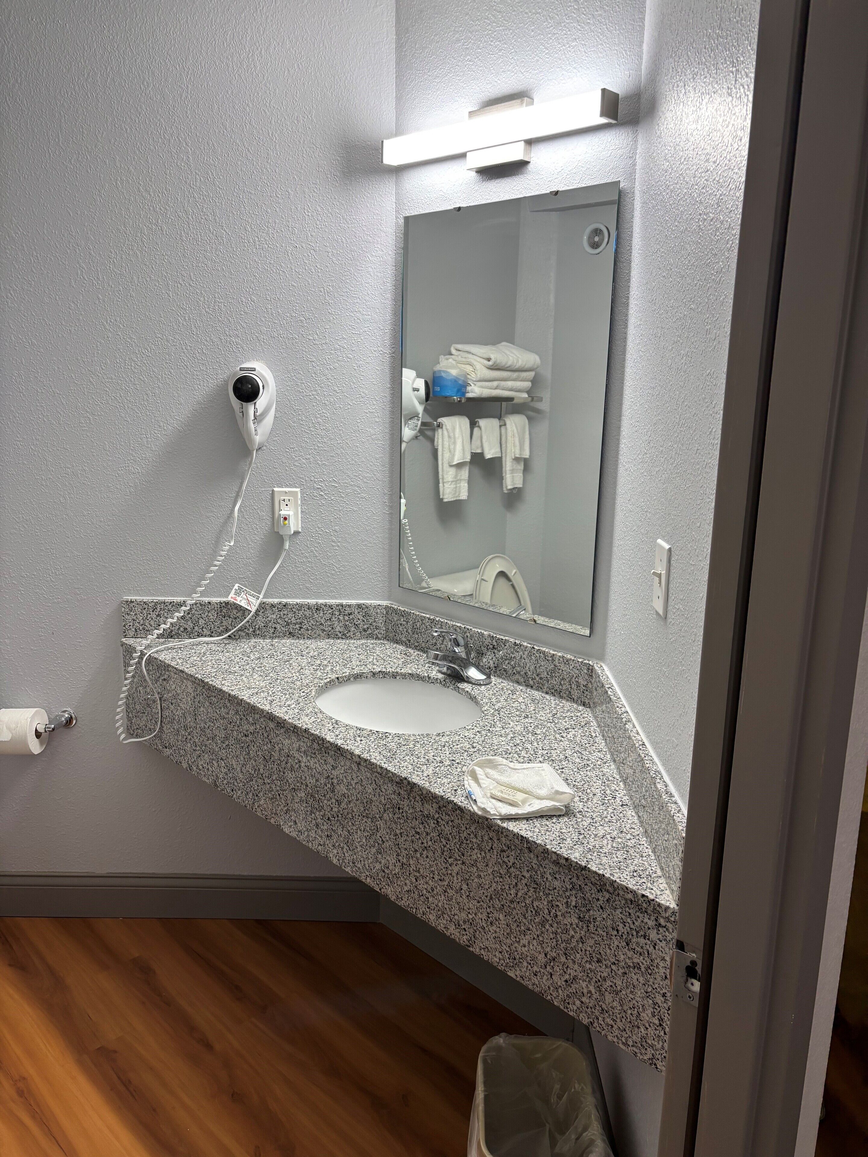 A bathroom with a granite countertop sink, a mirror, a hairdryer, and a towel rack.