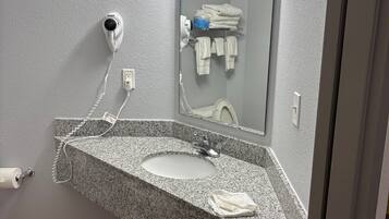 A bathroom with a granite countertop sink, a mirror, a hairdryer, and a towel rack.