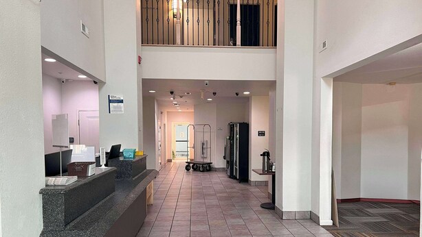 A hotel lobby with a reception desk, a second-floor balcony, and a tiled floor.