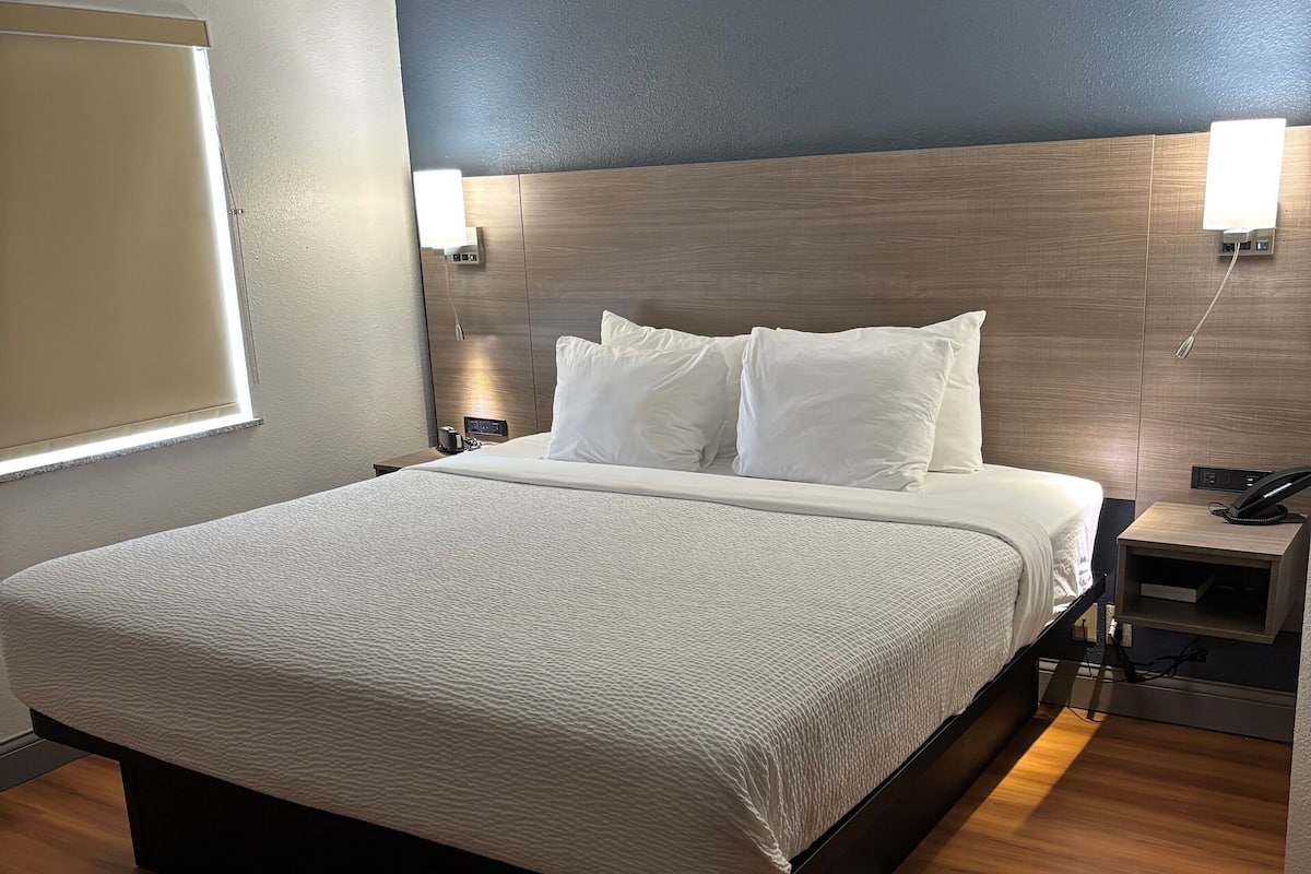 A hotel room with a large bed, wooden headboard, bedside lamps, and a nightstand with a phone.