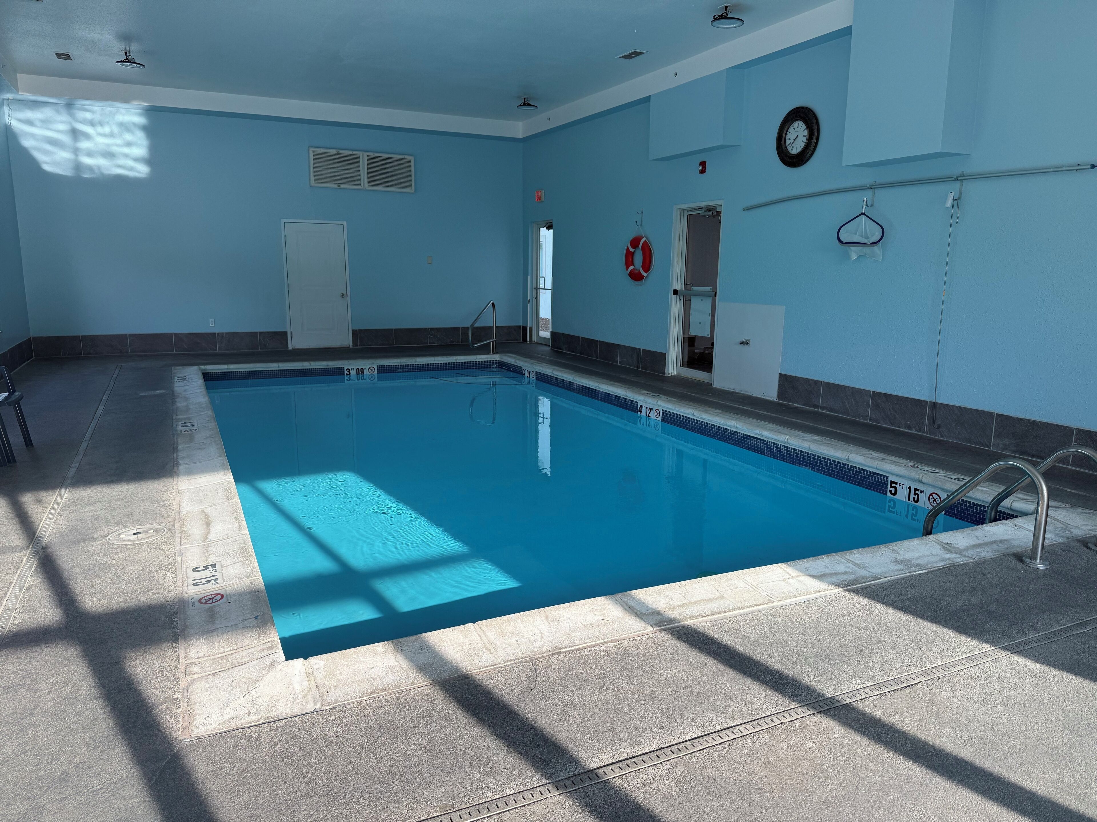 An indoor swimming pool with clear lane markings, a lifeguard chair, and a door leading to another room.