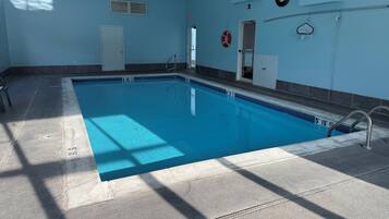 An indoor swimming pool with clear lane markings, a lifeguard chair, and a door leading to another room.