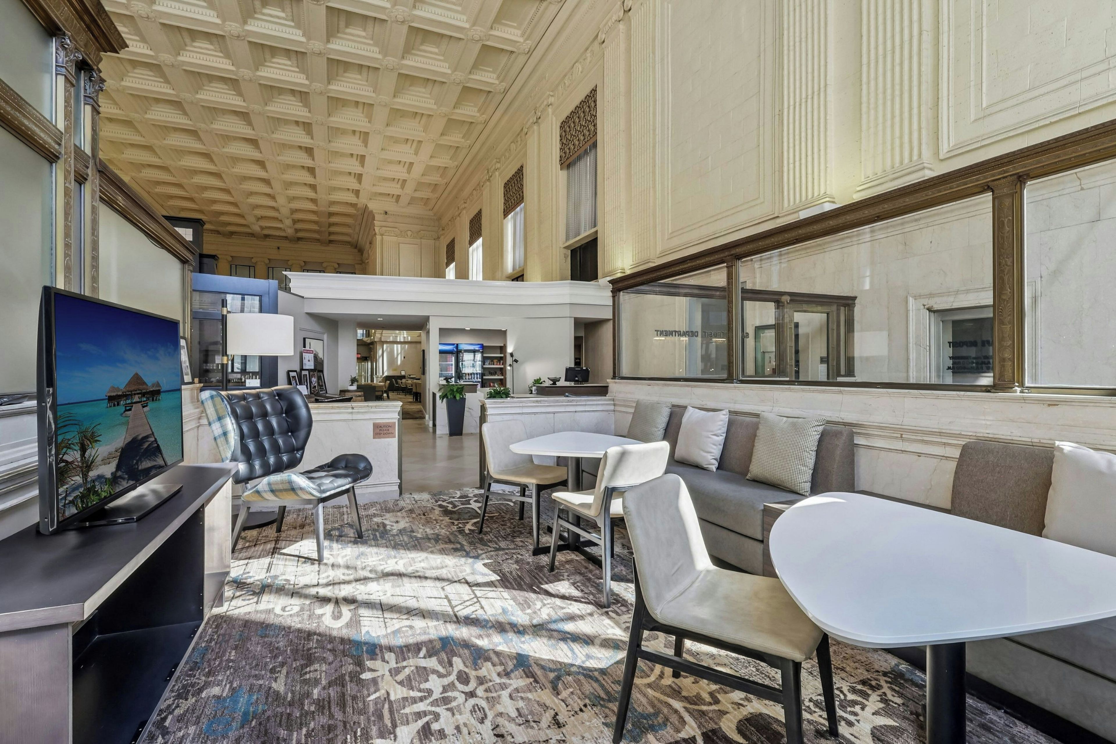 A spacious lobby with a high ceiling, a seating area with sofas and tables, and a television screen.