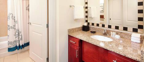 A bathroom with a white door, a shower curtain with a blue border, a sink with a granite countertop, and a mirror with a black and white frame.