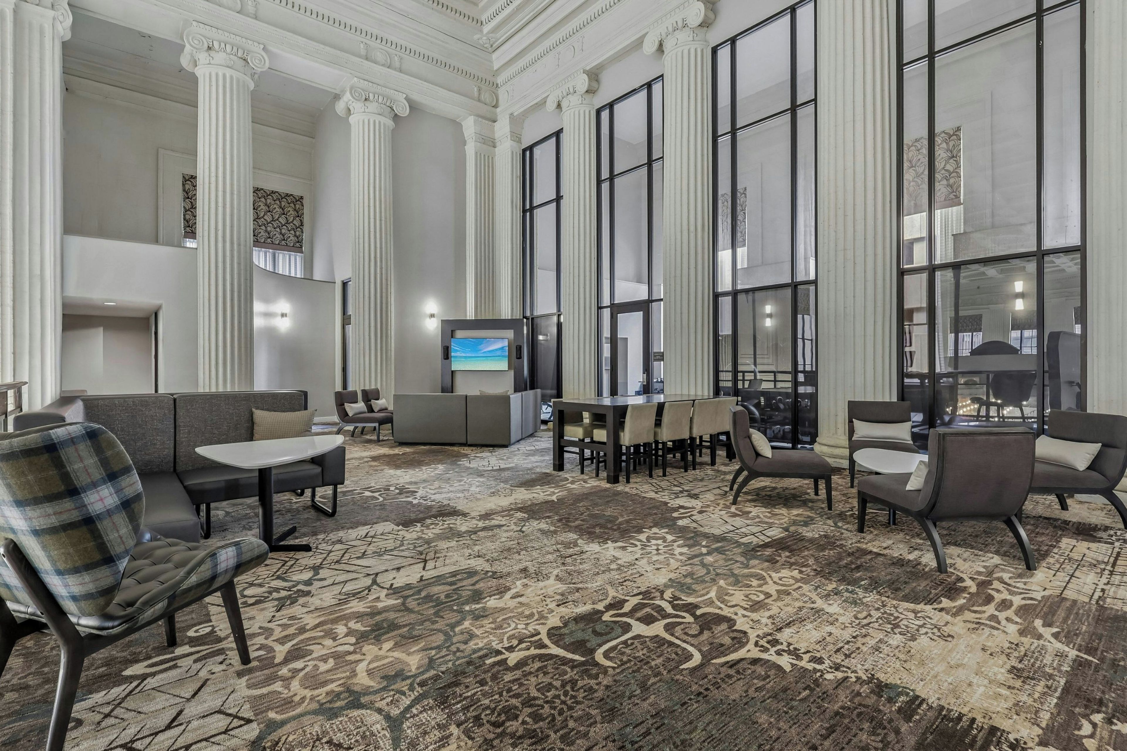 Un hall d’entrée spacieux, doté d’un plafond haut, de grandes fenêtres et d’un espace de détente central avec des canapés et des tables.