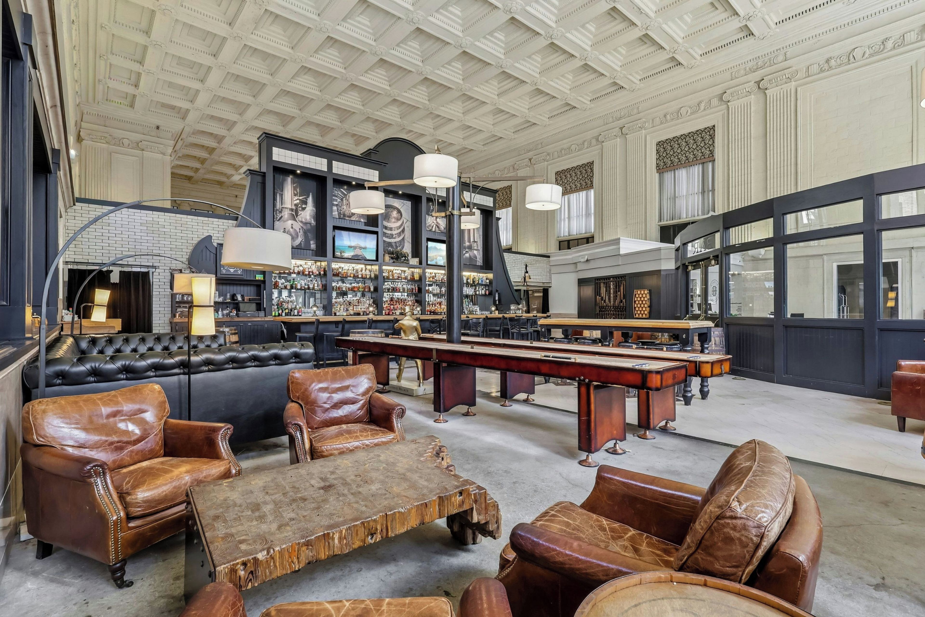 A spacious room with leather seating, a pool table, and a bar area with liquor bottles.