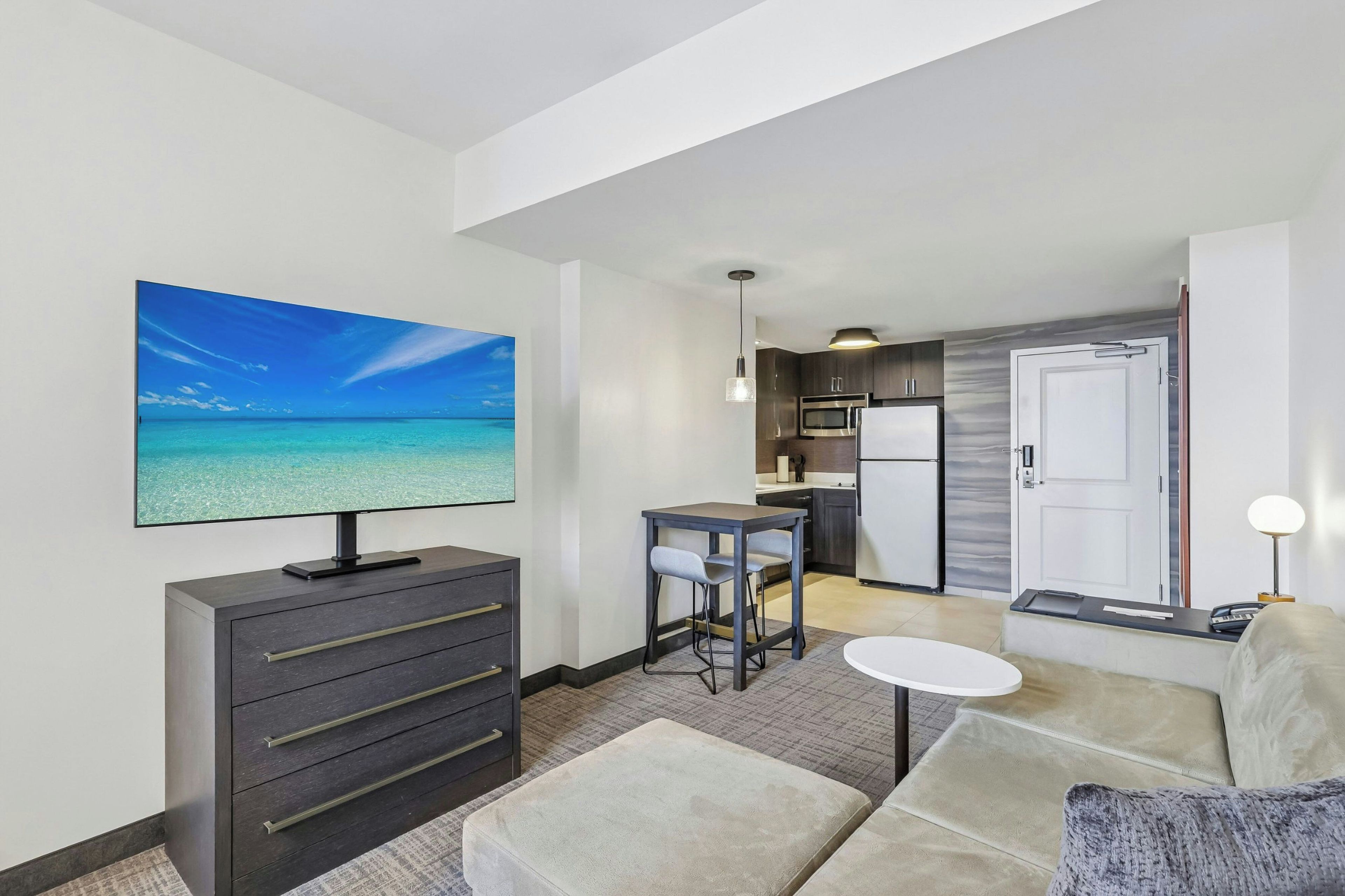 Habitación de hotel con televisión, sofá, una mesita, kitchenette y vista al océano.