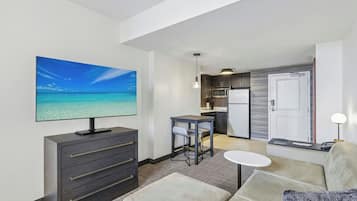 Habitación de hotel con televisión, sofá, una mesita, kitchenette y vista al océano.