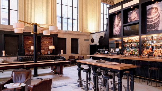 A spacious bar area with high ceilings and large windows, featuring a long counter with stools and a variety of bottles and glasses. - Residence Inn by Marriott Columbus Downtown (Columbus)