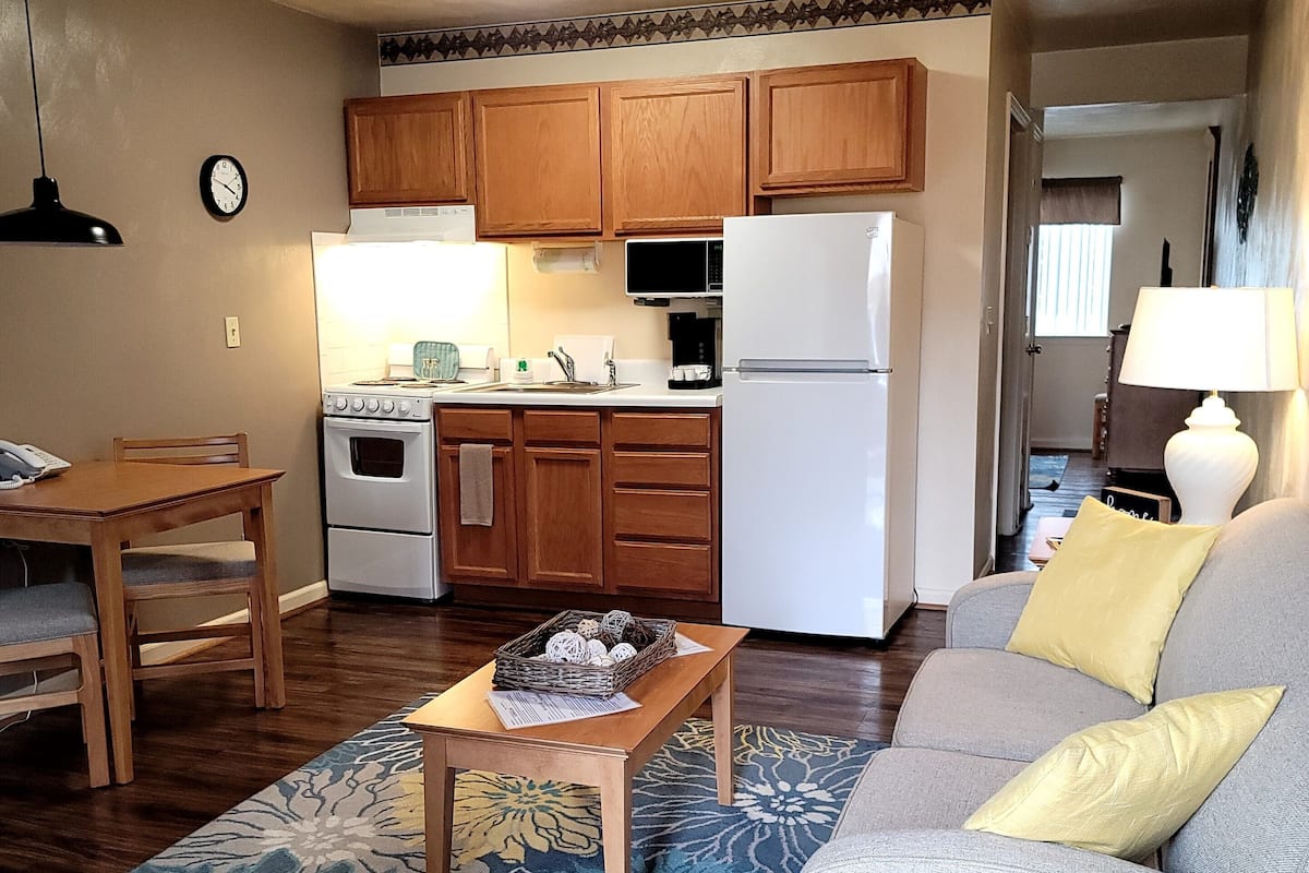 Un espacio habitable compacto con kitchenette, comedor y zona de estar con sofá y mesa de centro.