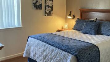 A bedroom with a bed, a nightstand, a lamp, and a window with blinds.