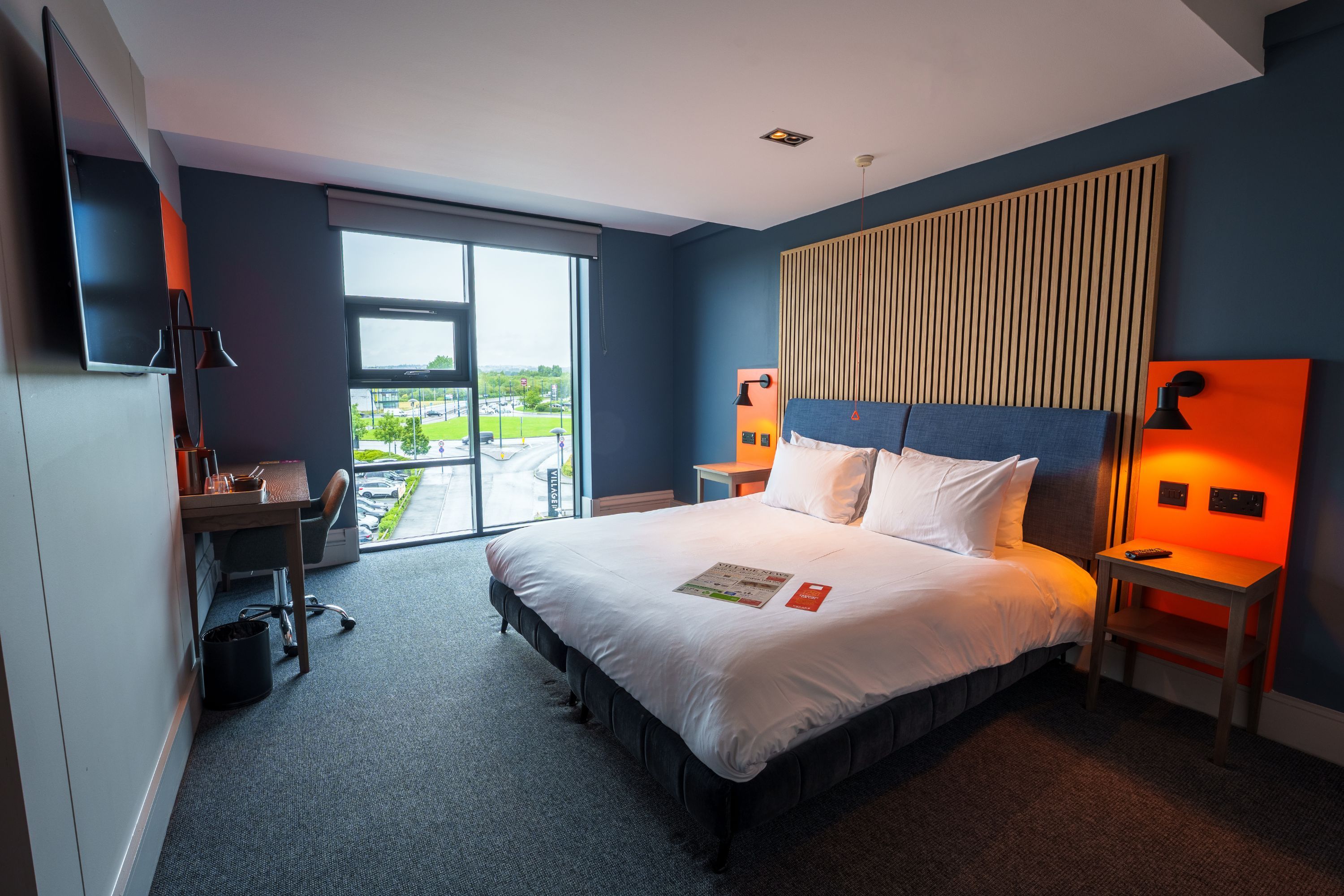 A hotel room with a large bed, a desk, a chair, a view of the outside, and a modern design.