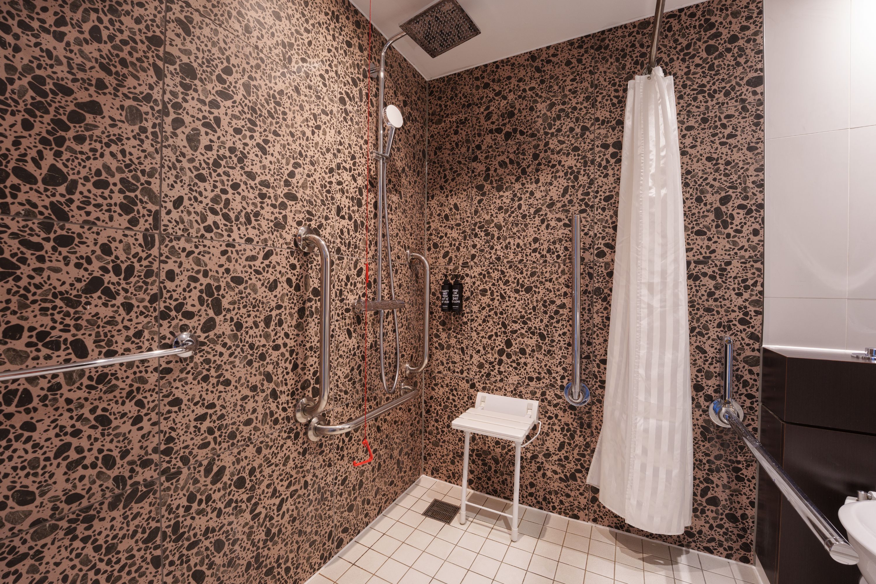 Ein modernes Badezimmer mit einer Wand mit Kieselstruktur, einer Dusche mit weißem Vorhang und einem kleinen, weißen Waschbecken.